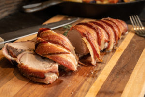 Bacon wrapped pork tenderloin on a cutting board.