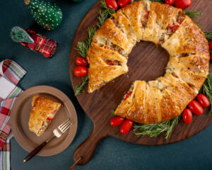 Holiday appetizer of ground hempler's sausage inside crescent rolls and shaped like a wreath. Holiday decorations surrounding the appetizer.