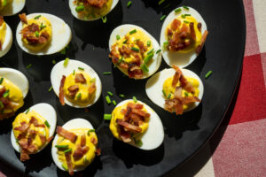 Deviled eggs with Hempler's bacon and chives on a black plate.