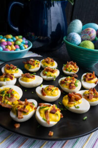 Deviled eggs with chives and Hempler's bacon on a black plate with Easter decorations.