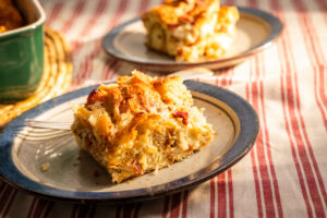 Slice of bacon croissant breakfast casserole made with Hempler’s Center Cut Bacon, served on a plate with flaky croissants, eggs, and melted cheese in warm morning light