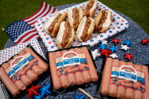 Hot dogs 4th of July themed with blue table, American flag, hot dogs with onions and cream cheese.