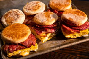 A tray of English muffin breakfast sandwiches featuring Hempler's European bacon, eggs and cheddar cheese.