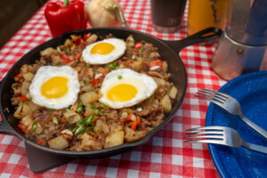 Plaid picnic table cloth with a cast iron skilled full of breakfast hash made with sausage. The dish is topped with 3 eggs cooked over easy.