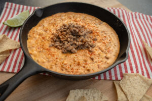 Cast iron skillet with queso and Hempler's pork sausage dip. Served with potato chips and a sliced lime on the side.