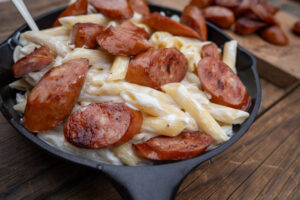Cast iron skillet with white cheddar macaroni and cheese topped with grilled smoked sausages.