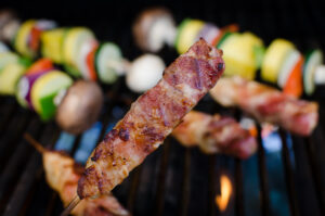 Chicken skewers over a grill with skewered vegetables behind it